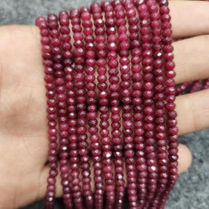 May include: Strands of faceted, deep red beads. The beads are small and uniform in size, strung together to create a flowing, textured appearance. The color is a rich, saturated red, with a slight sparkle from the facets.