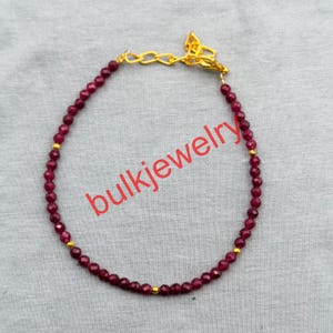 Peut inclure: Un bracelet de perles composé de petites pierres facettées rouge foncé disposées en cercle. Le bracelet comprend de minuscules perles intercalaires en métal doré et un fermoir mousqueton en métal doré avec une chaînette d'extension.