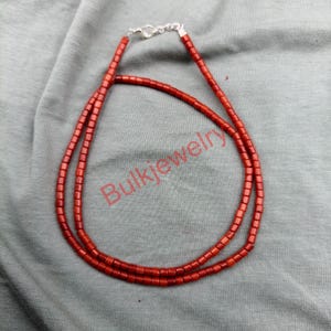 Op de afbeelding: Een rode kralenketting met een zilveren sluiting. De ketting is gemaakt van kleine, rechthoekige kralen. De tekst "Bulkjewelry" is zichtbaar in de afbeelding. De ketting wordt gepresenteerd op een grijze ondergrond.