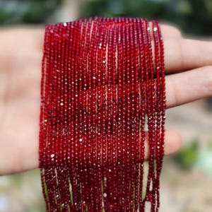 May include: A close-up of a collection of deep red gemstone beads. The beads are strung together, creating a cascading effect. The color is a rich, vibrant red, and the beads appear to be small and uniform in size. Suitable for jewellery making.