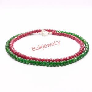 Puede incluir: Un collar que presenta dos hilos de pequeñas cuentas redondas facetadas. Un hilo consiste en cuentas de color rojo intenso, mientras que el otro hilo está compuesto por cuentas de color verde vibrante. Los hilos están unidos por un cierre de metal plateado. El texto Bulkjewelry es visible.