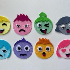 May include: Eight circular felt appliqués featuring diverse cartoon faces with distinct expressions. The set includes yellow, pink, green, grey, blue, purple, orange, and bright pink characters, each with unique hair colours and facial features.
