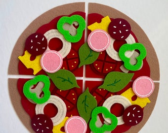 May include: A felt pizza divided into four slices with various toppings including green peppers, red pepper, white onion, pink ham, cheese, and basil.