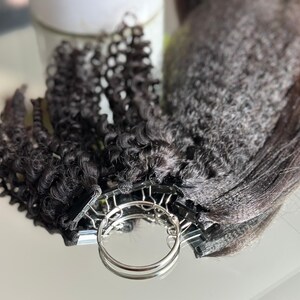 Puede incluir: Un conjunto de extensiones de cabello humano negro con una variedad de texturas, incluyendo liso, ondulado y rizado. Las extensiones están sujetas a un sistema de clip plateado.