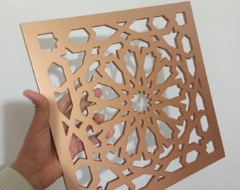 May include: A square, copper-colored metal wall decor with a geometric, intricate design. The design features a repeating pattern of stars and circles.