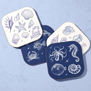 May include: Set of four square coasters with rounded corners. Two coasters are white with blue seashell illustrations. The other two are navy blue with illustrations of sea creatures, including a crab, octopus, and seahorse.