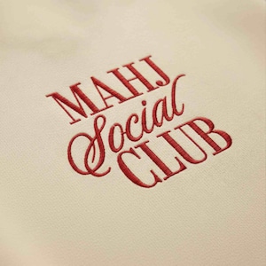 May include: Cream-colored fabric with embroidered text in red. The text reads "MAHJ Social CLUB" in a mix of serif and script fonts. The embroidery is detailed and the fabric has a subtle texture.