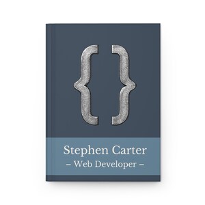 May include: A notebook with a dark blue cover and a silver bracket symbol. The bottom section of the cover has the name "Stephen Carter - Web Developer -" in white text.