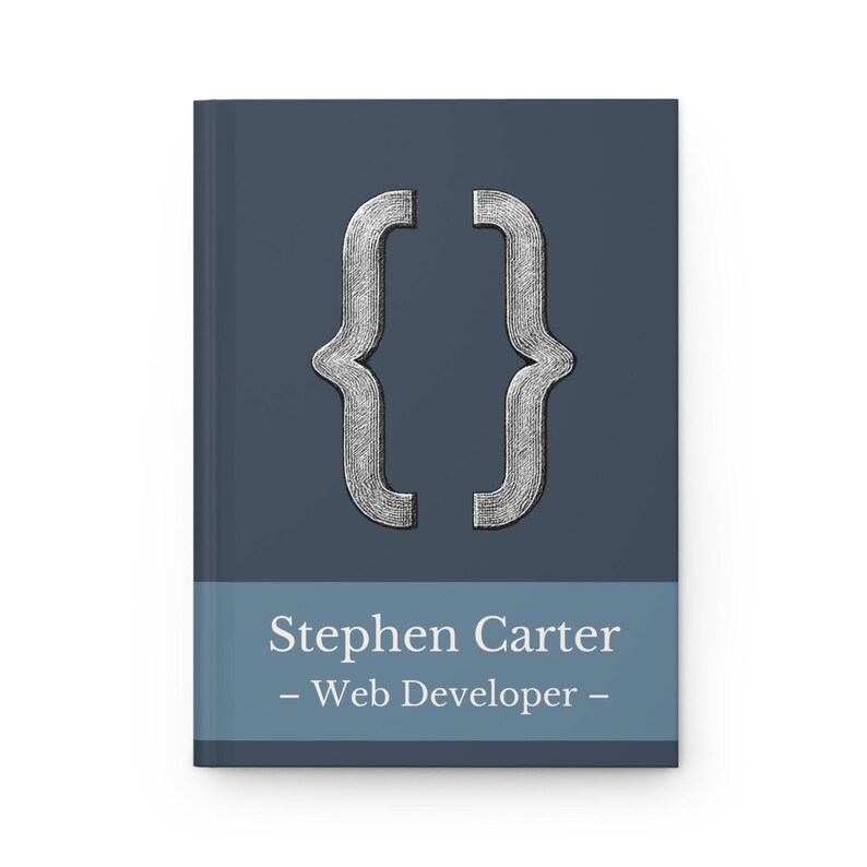 May include: A notebook with a dark blue cover and a silver bracket symbol. The bottom section of the cover has the name "Stephen Carter - Web Developer -" in white text.