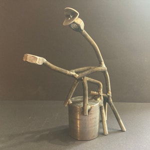 May include: A metal sculpture of a figure made from nuts and bolts. The figure is sitting on a metal base.