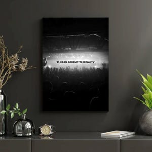 Puede incluir: Impresión en blanco y negro enmarcada que representa una escena de concierto con una multitud e iluminación del escenario. El texto "THIS IS GROUP THERAPY" es visible. La impresión está en una pared gris oscuro.