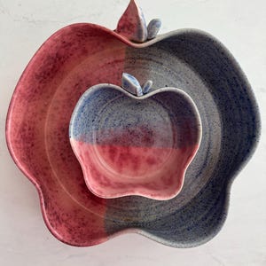 Puede incluir: Un juego de tres fuentes de cerámica con forma de manzana. La fuente más grande está dividida en secciones rojas y azules. La fuente mediana es azul y roja, y la más pequeña es azul y roja. Las fuentes tienen un acabado texturizado.