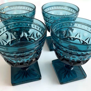 May include: Set of four teal blue glass cups with a square base and a diamond pattern.