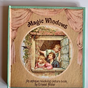 May include: A vintage children's book titled "Magic Windows" by Ernest Nister. The cover features a circular illustration of three children looking out a window with a bird flying by. The book is bound in green and brown with a pink and white curtain design.