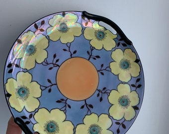May include: A blue and yellow floral patterned serving plate with two black handles. The plate has a iridescent glaze.