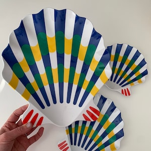 May include: Three white ceramic seashell-shaped serving dishes with blue, green, yellow, and red stripes and dots.