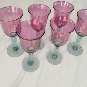 Pode incluir: Seis taças de vinho cor-de-rosa com bordas douradas e hastes e bases azuis claras. As taças estão dispostas em grupo, mostrando seu design elegante. Ideais para servir vinho ou outras bebidas.