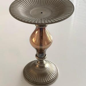 Puede incluir: Un candelero de metal plateado con una parte superior redonda y estriada y una base de vidrio transparente con un acabado iridiscente dorado y azul.