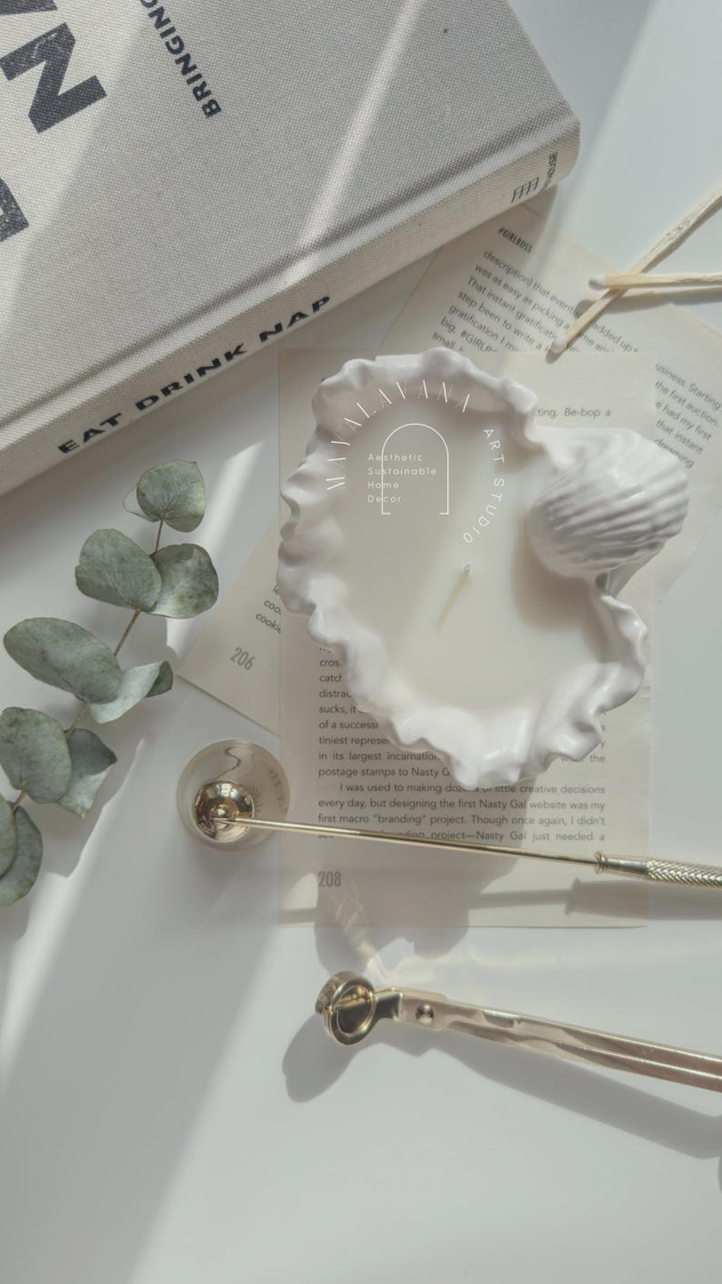 May include: A white ceramic candle holder shaped like a seashell with a white candle inside. The candle holder has a ruffled edge and a small seashell on top. The text "Aesthetic Sustainable Home Decor" is written on the candle holder.