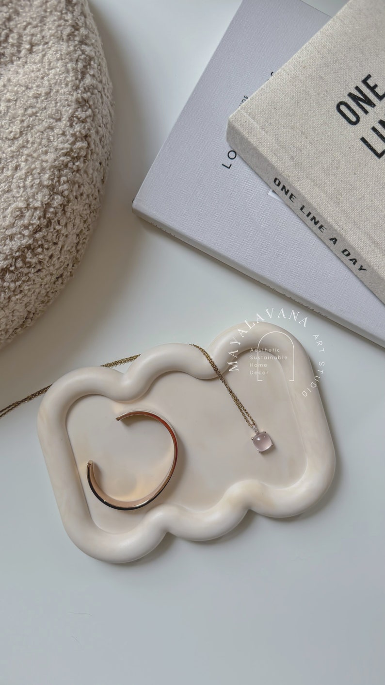 May include: A white ceramic tray with a cloud-like shape, featuring a gold bracelet and a delicate necklace with a pink gemstone pendant. The tray is labelled "MAYALAVANA ART STUDIO" and "Aesthetic Sustainable Home Decor".