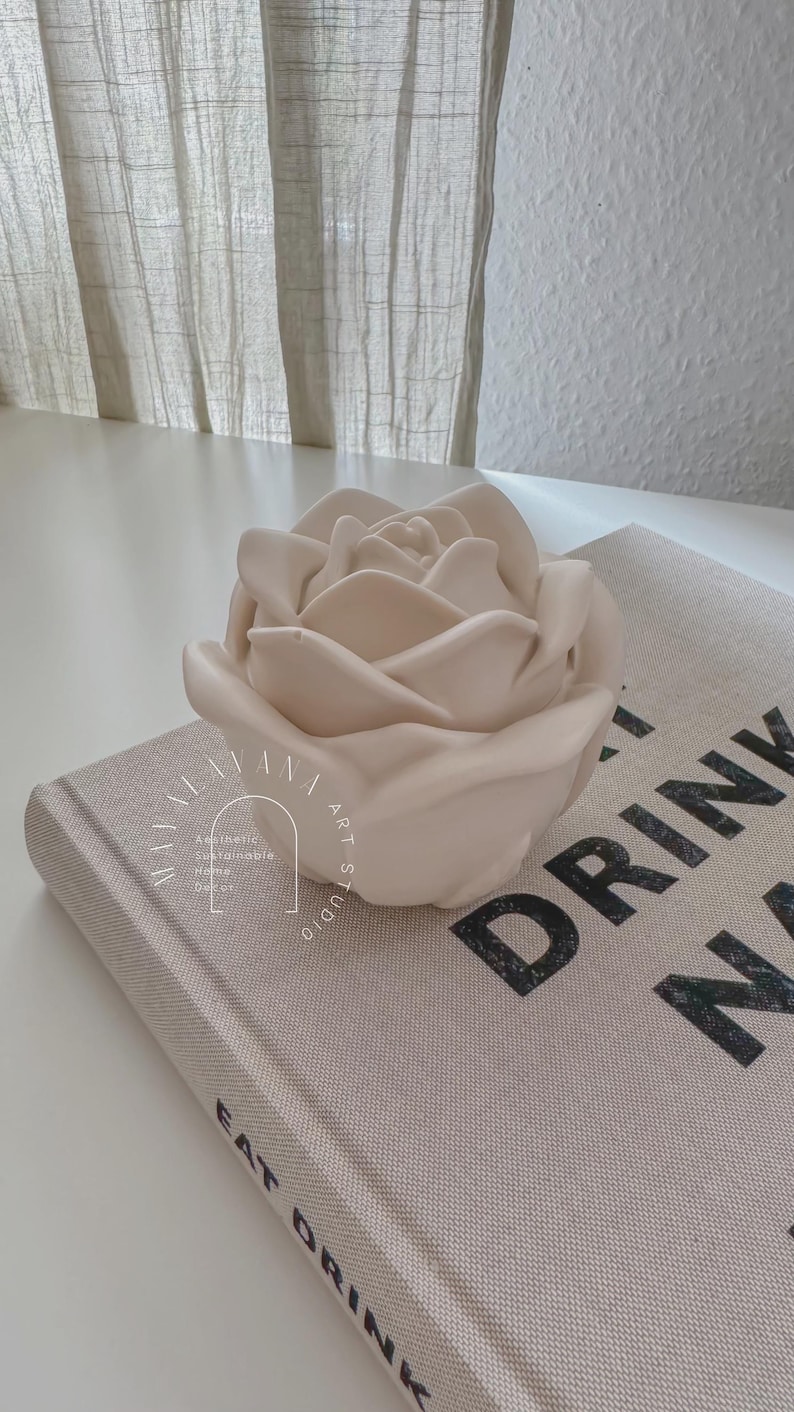 May include: A light pink ceramic rose sculpture on top of a book with the text "Eat Drink" and "Drink Nap" printed on the cover.