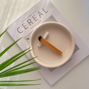 Könnte beinhalten: Eine beige Keramik Schale mit einem Holzstäbchen-Räucherstäbchen darin. Die Schale liegt auf einem Magazin mit dem Titel "Cereal" und dem Text "Travel & Style Guide" darunter.