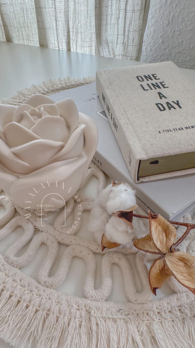 May include: A white ceramic rose sits on a white woven rug with a book titled "One Line a Day: A Five-Year Memory Journal" and a cotton boll.
