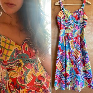 May include: A colorful, abstract print midi dress with a sweetheart neckline and button closures. The dress is made of a lightweight fabric and has a flowy silhouette.