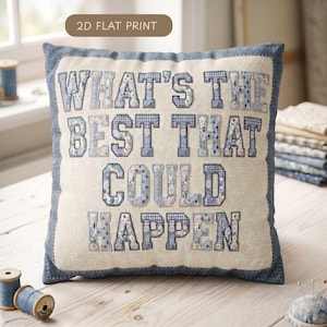 May include: Square decorative pillow with the text "WHAT'S THE BEST THAT COULD HAPPEN" in blue and white patterned letters. The pillow has a light beige background and a blue border. The words are in a collegiate style font.