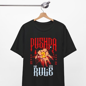 May include: Black t-shirt with a red graphic of a hand with the number 2 on it. The text "Pushpa" and "The Rule" are also on the shirt.