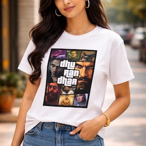 May include: White t-shirt with a graphic design featuring the text "dhu ran dhan" and various faces. The shirt is paired with blue jeans. The model is wearing gold hoop earrings and a gold bracelet.