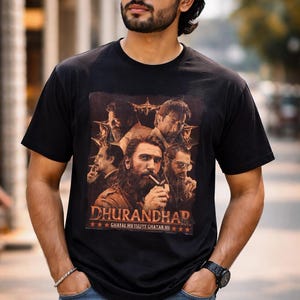Może przedstawiać: Czarny t-shirt z pomarańczową grafiką przedstawiającą kilku mężczyzn i napisem "DHURANDHAR". Koszulka jest noszona przez osobę noszącą okulary przeciwsłoneczne i niebieskie dżinsy.