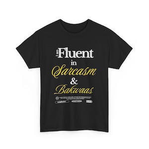 Puede incluir: Camiseta negra con el texto "I am Fluent in Sarcasm & Bakwaas" en letras blancas y amarillas. La camiseta también incluye el texto "Every choice, every step, weaves the narrative of your life. Decide thoughtfully, for each moment shapes..." y el nombre de la marca.