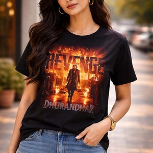 May include: Black t-shirt featuring a movie poster design with the words "THE REVENGE" and "DHURANDHAR" in a fiery, action-packed scene. The shirt is paired with blue jeans.