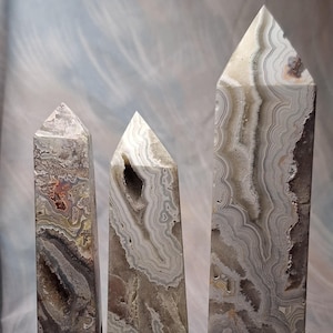 May include: Three agate crystal points, varying in size, with a white, gray, and brown banded pattern. The points are arranged in a row from largest to smallest, with a US quarter coin for scale.