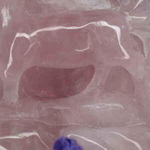 May include: A pink quartz sculpture of a cow standing on a base. The sculpture is carved with intricate details and has a smooth, polished finish.