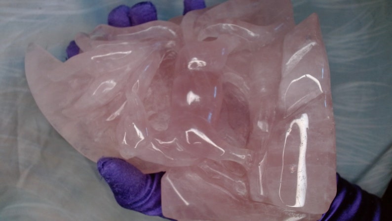 May include: A large, intricately carved pink rose quartz sculpture. The sculpture is smooth and polished, with a translucent appearance.