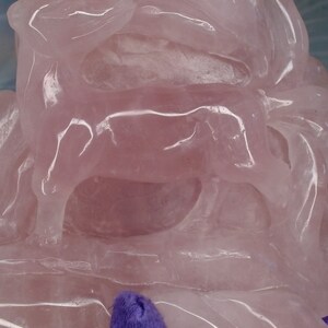 May include: A pink rose quartz sculpture of a cow, carved in a layered style. The sculpture is polished and translucent, with light shining through the stone.