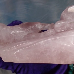 May include: A carved pink rose quartz sculpture of a reclining figure. The sculpture is smooth and polished, with a translucent appearance.