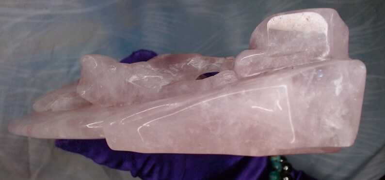 May include: A carved pink rose quartz sculpture of a reclining figure. The sculpture is smooth and polished, with a translucent appearance.