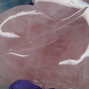 May include: A large, pink, heart-shaped piece of rose quartz with white veins and swirls. The quartz is polished and smooth.