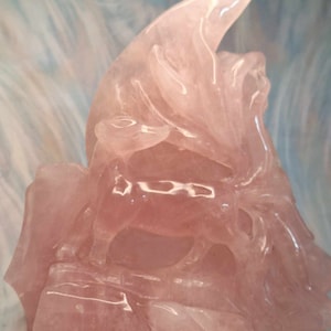 May include: A pink rose quartz carving of a mythical creature, possibly a dragon or griffin, with intricate details and a smooth, polished finish.