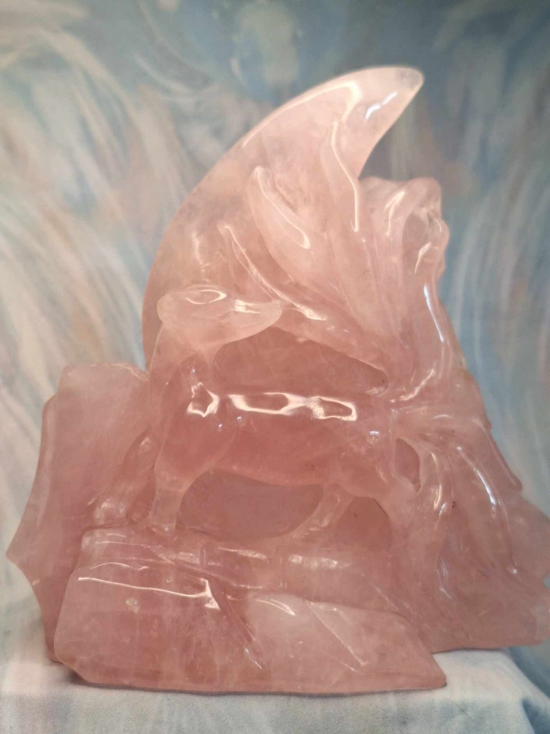 May include: A pink rose quartz carving of a mythical creature, possibly a dragon or griffin, with intricate details and a smooth, polished finish.