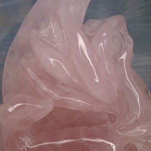 May include: A pink rose quartz carving of a stylised flower with intricate details. The carving is made of polished rose quartz, which gives it a smooth, glassy finish.