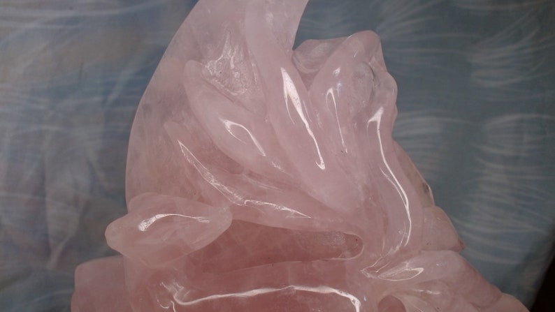 May include: A pink rose quartz carving of a stylised flower with intricate details. The carving is made of polished rose quartz, which gives it a smooth, glassy finish.
