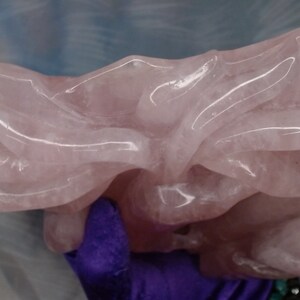 May include: A large, intricately carved rose quartz sculpture. The sculpture is a light pink colour and has a smooth, polished finish.