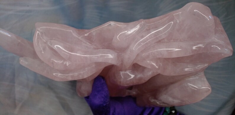 May include: A large, intricately carved rose quartz sculpture. The sculpture is a light pink colour and has a smooth, polished finish.