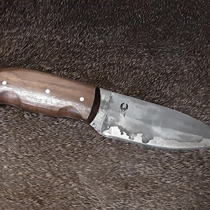 May include: A handcrafted knife with a dark wooden handle and a silver blade. The handle has three white rivets. The blade has a unique, textured appearance and a small emblem near the handle.