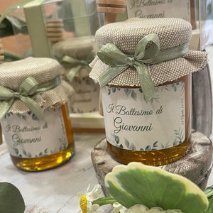 Peut inclure: Petits pots en verre de miel, décorés de toile de jute et d'un ruban vert. Les pots portent des étiquettes indiquant "Il Battesimo di Giovanni" et la date "28 Aprile 2024".
