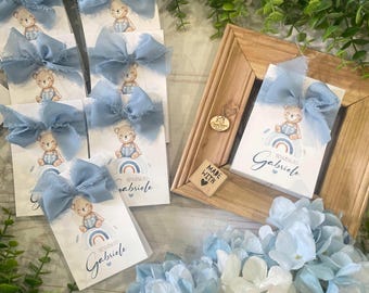 May include: Rectangular white cards featuring a cartoon bear sitting on a rainbow with the text Benvenuto Gabriele, each topped with a frayed light blue chiffon ribbon bow. One card is displayed inside a light wood frame with a small wooden tag.